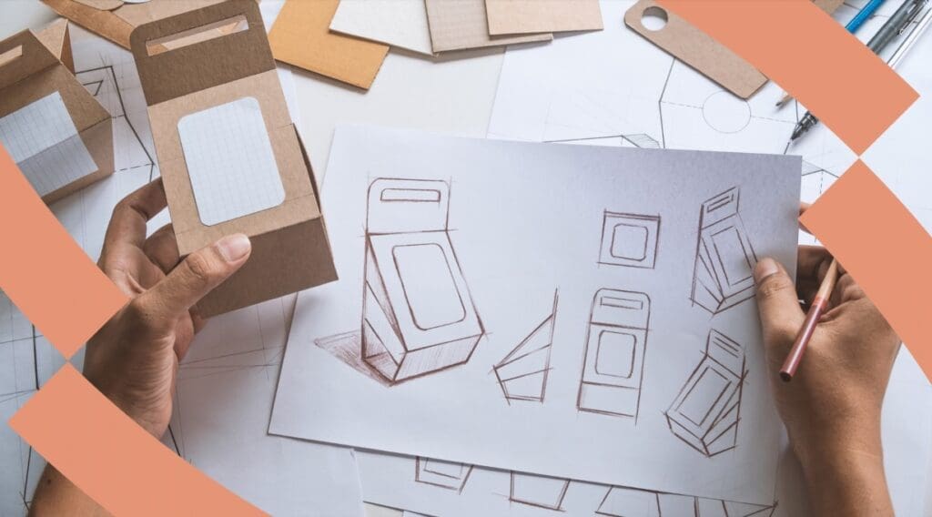 Two hands at a desk, one holding a cardboard package the other a pencil drawing packaging designs onto a sheet of paper.