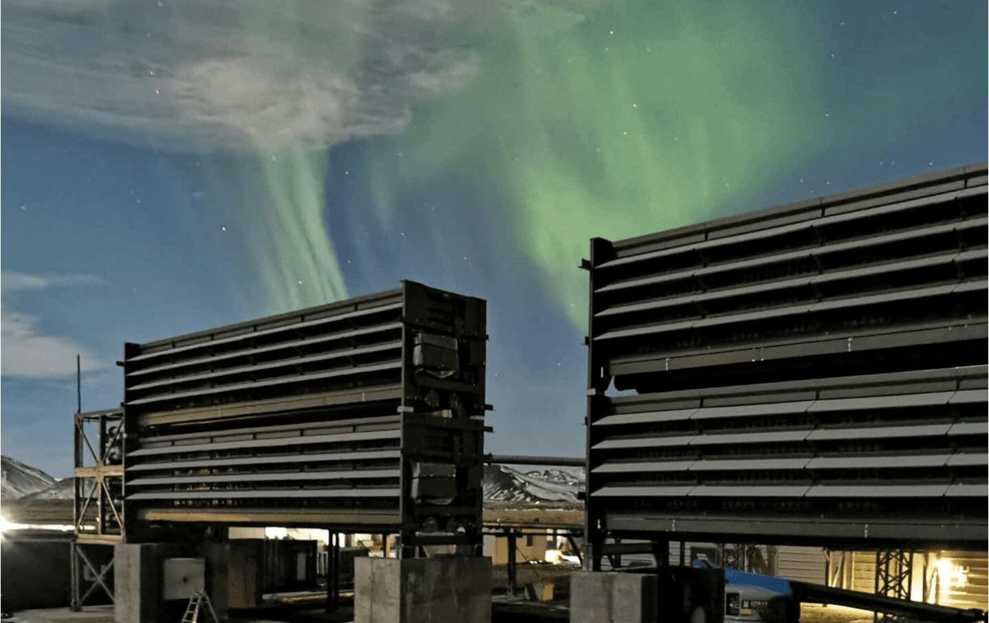 two buildings stand against dark sky with clouds of green light emanating from their roof tops.