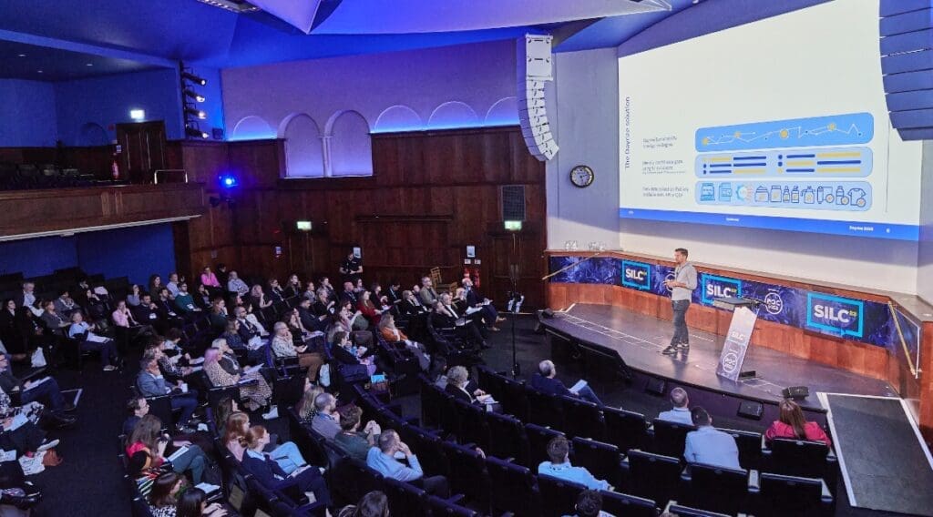 Member of the Dayrize team stands on stage in front of large screen showcasing product impact measurement tools.