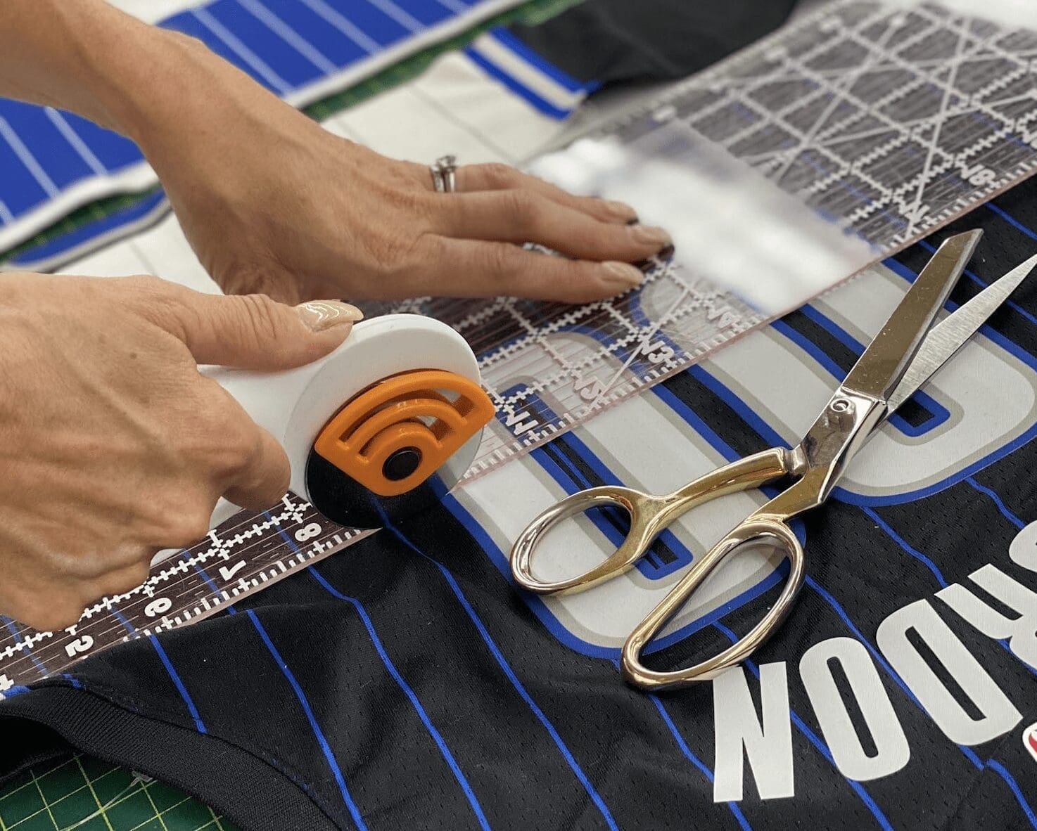 hands at a textile cutting table score a branded sports t shirt along a ruler with a pair of scissors