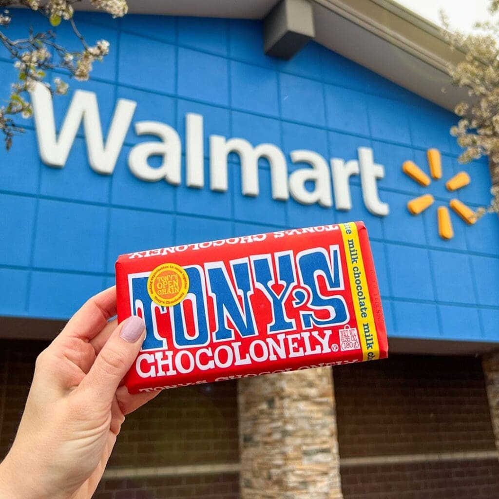 a hand holds aloft a bar of Tony's Chocolonely chocolate in front of the outdoor Walmart sign