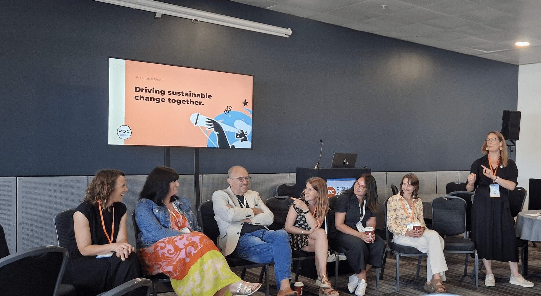 row of people sat smiling in chairs in front of a TV screen on the wall projecting the POC homepage.