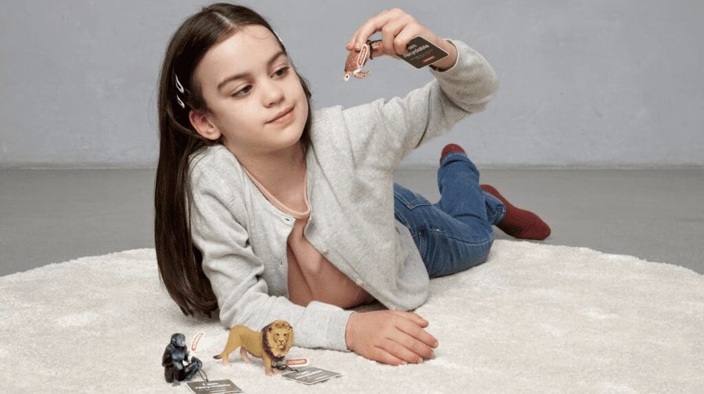 A girl lays playing on the floor with a toy turtle, a bonobo, and a lion.