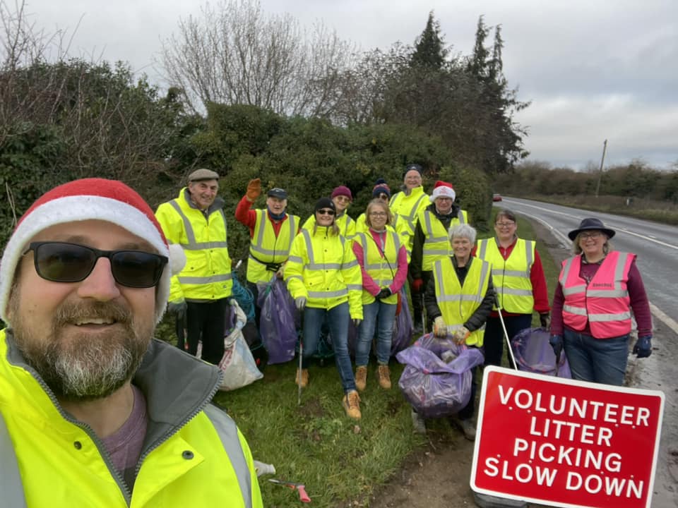 A group of people stand together in high-vis by the side of the road with litter picking equipment.