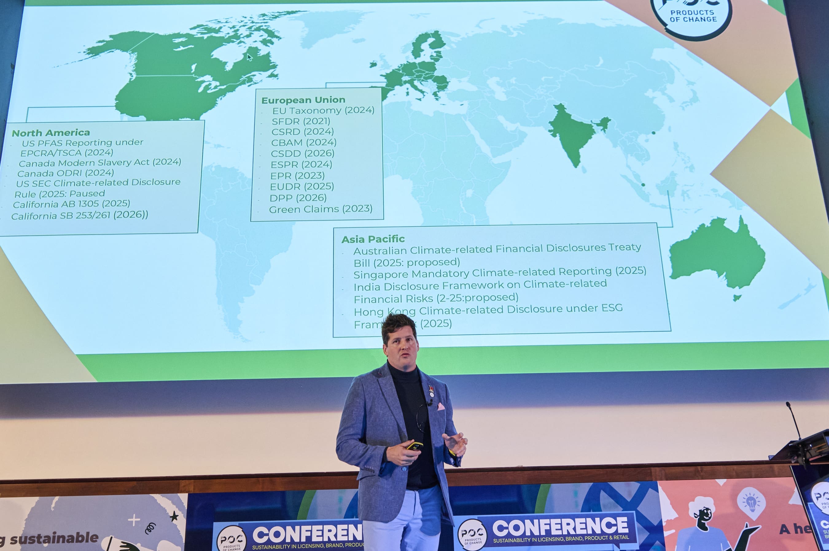 James George stands on stage in front of a screen that has a map of the world on it with list of legislations.