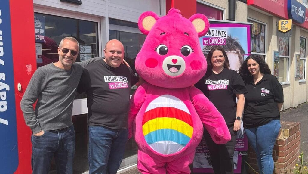 A Care Bare mascot with four people posing and smiling outside a OneStop