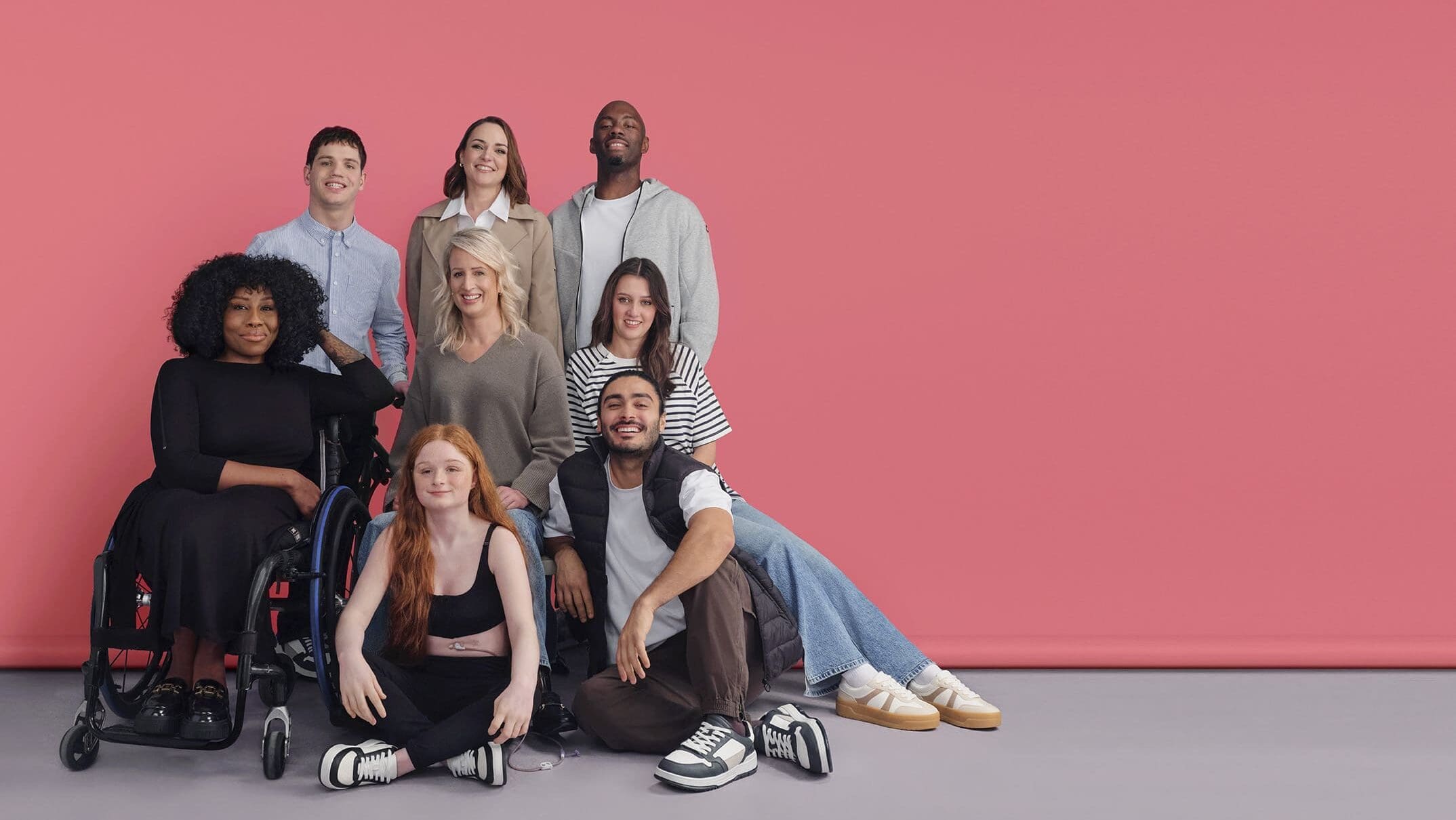 A group of people modelling the adaptive fashion rnage on a pink background.